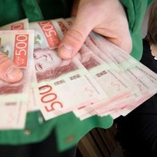 Pengar i handen och en kvinna vid en dator.