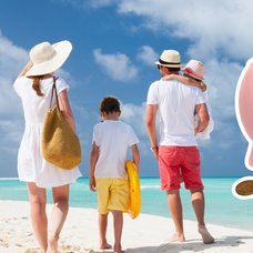 En familj på en strand i bakgrunden. En utklippt spargris med mynt runt sig till höger.