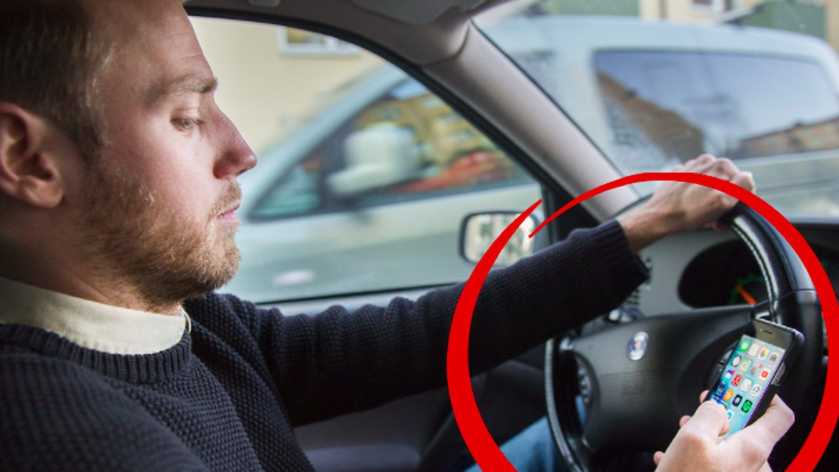 Man som tittar ner i sin mobil när han kör bil.