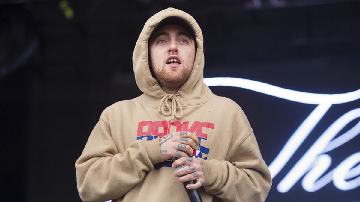Mac Miller i beige tröja håller i en mikrofon.