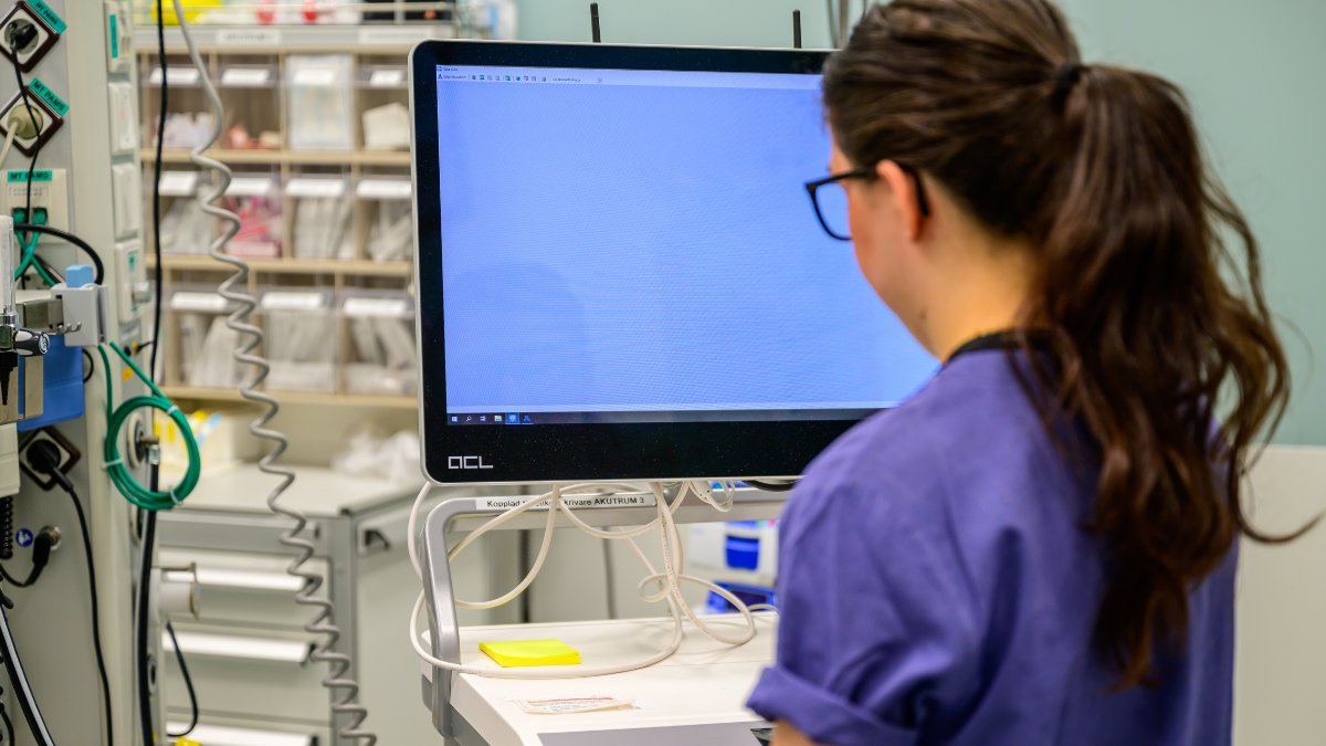 En kvinna som är sjuksköterska tittar på en dator i en vårdcentral.