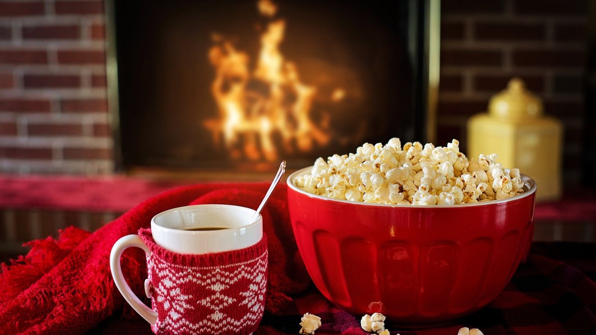 Mugg, röd skål med popcorn, brasa i bakgrunden. 
