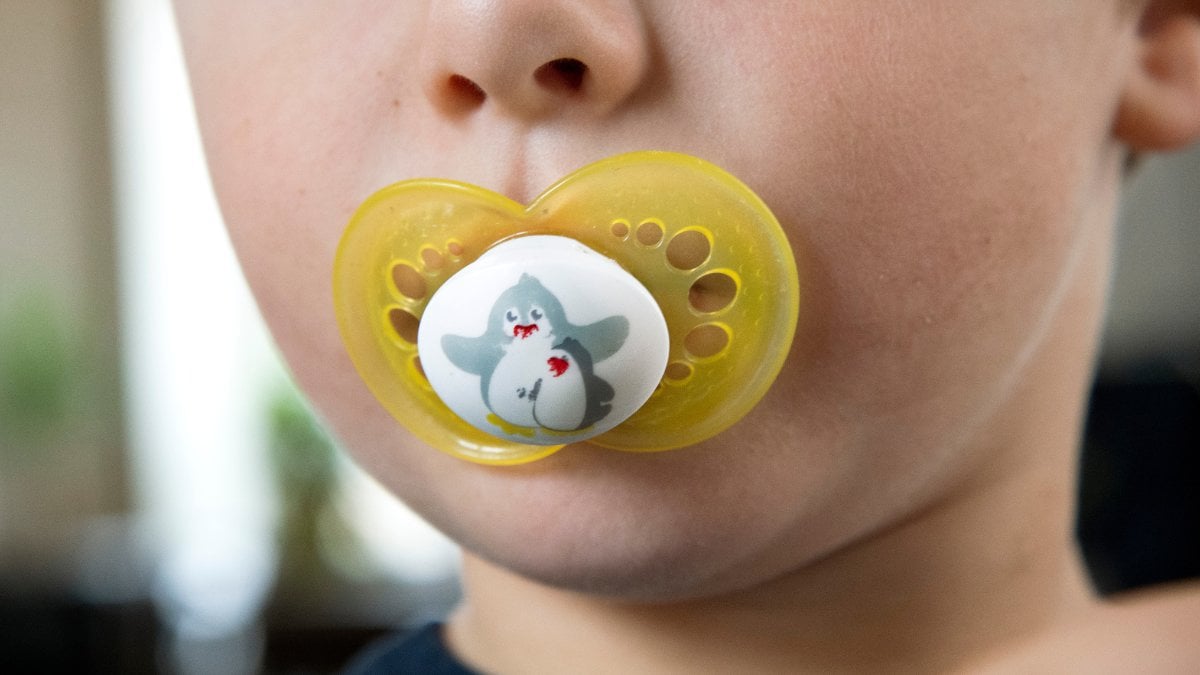 Ett barn med en gul napp i munnen.