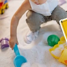 Barn i en sandlåda med leksaker i bakgrunden. Asbest-skylt utklippt till höger.