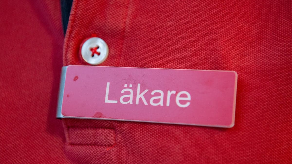 En person med en skylt som lyder: Läkare, på bröstet.