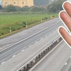 E22:an norr om Lund i bakgrunden. En hand som signalerar stopp utklippt höger.