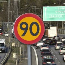 Hastighetsskylt och en motorväg med lastbilar och bilar.