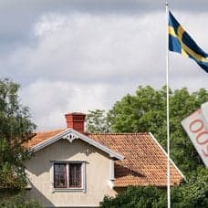 Hus med flaggstång och svenska flaggan, samt en hand med 500-lappar i.