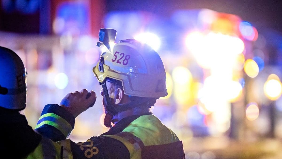 En brandman framför en eld med blålljus i bakgrunden.