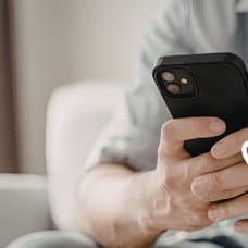 Person som hålle ri en mobil i bakgrunden. Händer som håller en plånbok och tar ut kontanter ur den höger.