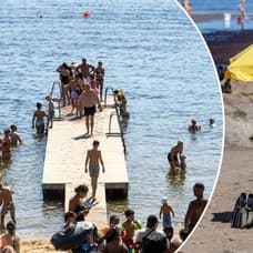 En strand med ett äldre par under ett parasol och en badbrygga.