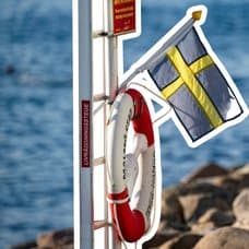 Svensk flagga och livboj vid vattnet.