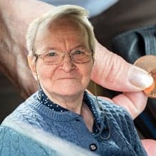 En äldre person i förgrunden och i bakgrunden en person som håller i en plånbok med ett par mynt i.