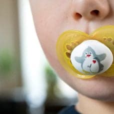 Ett barn med en gul napp i munnen.