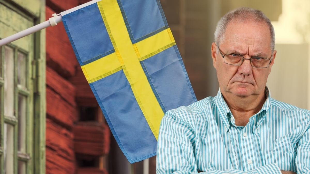 Svenska flaggan på en fasad och en man med korsade armar som ser arg ut.