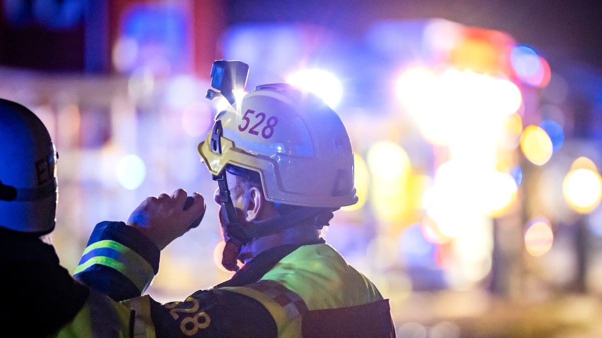 En brandman framför en eld med blålljus i bakgrunden.