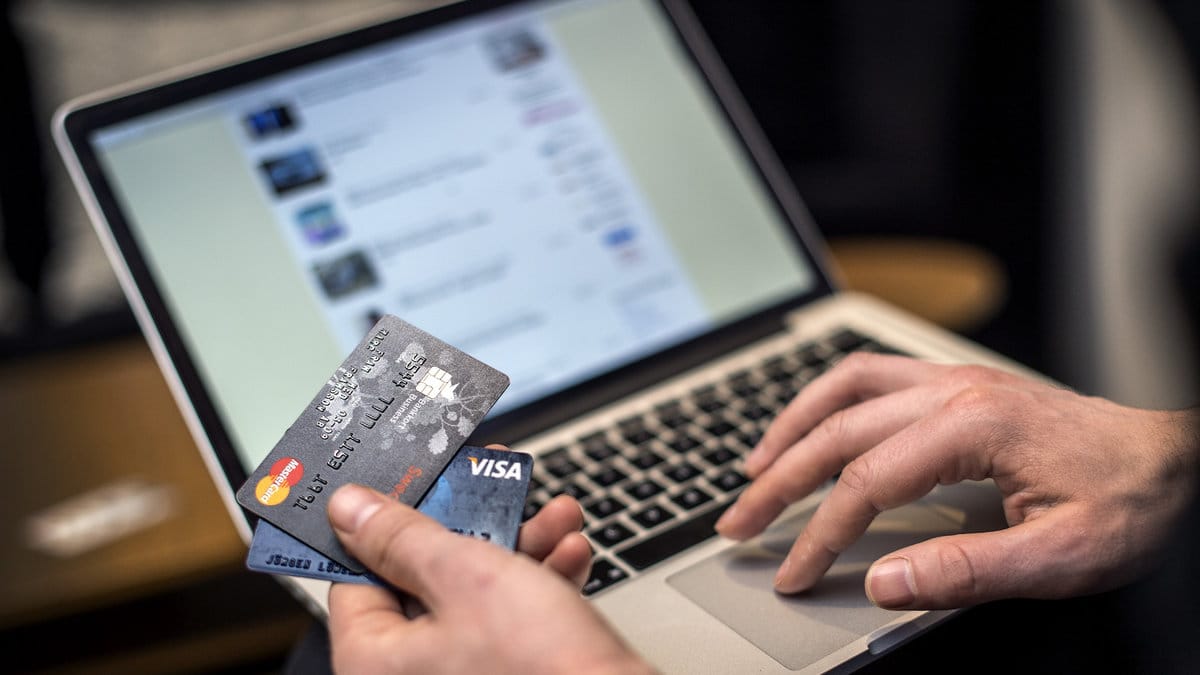 Person sitter vid datorn med kreditkort i handen